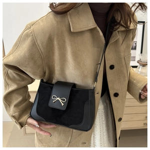 Detail of black crossbody bag with mixed leather textures and golden bow metal buckle