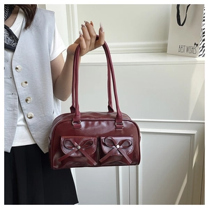 Close-up of wine red faux leather shoulder bag with decorative bows and front flap pockets