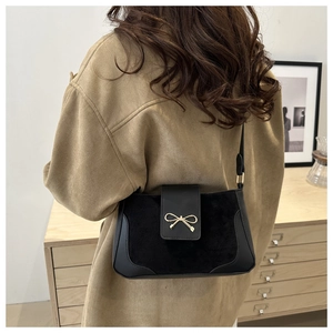 Detail view of black saddle bag with gold bow buckle on model in brown wool coat