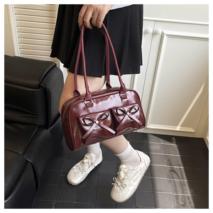 Detail of dark burgundy shoulder bag featuring dual bow accents and sleek PU leather texture