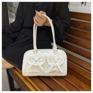 Detail of white Boston bag featuring delicate bow accents on front flap pockets