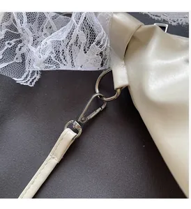 Détail macro de la boucle en métal argenté et de la dentelle fine sur le sac crème