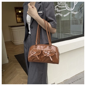 Detailed close-up of brown leather underarm bag with decorative bows on a model