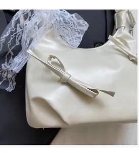 Détail du sac à main crème avec nœud sur un blazer noir et fond en dentelle blanche