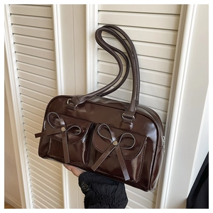 Detail of dark brown leather shoulder bag featuring bow accents and functional pockets