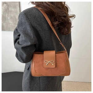 Close-up of a brown shoulder bag featuring a golden bow buckle and mixed textures