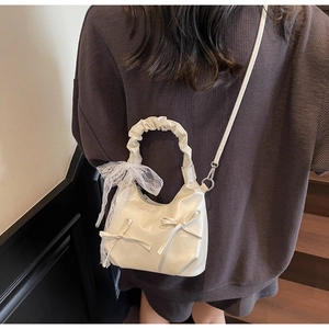 Détail du ruban en dentelle sur un sac hobo plissé blanc porté en bandoulière