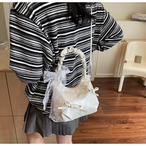 Detail of a creamy white crossbody bag featuring lace bow accents and pleated handle