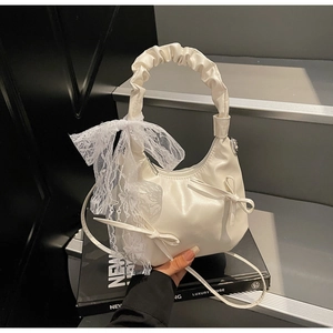 Close-up of white leather crescent handbag featuring elegant lace bows and ruched handle detail