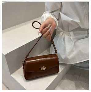 Detail of dark brown leather crossbody bag featuring a golden metal twist lock closure