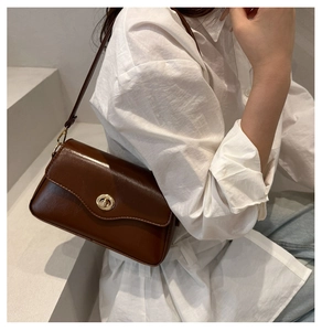 Detail of dark brown leather shoulder bag featuring a golden circular twist lock closure