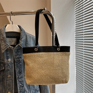 Straw woven tote bag with black leather straps hanging on a display for summer style