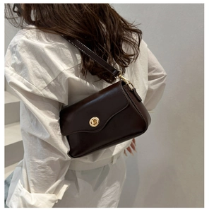 Detail of a deep brown shoulder bag with golden round turn-lock on premium faux leather