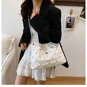Detailed view of white quilted faux leather bag with star emblem and chain strap on shoulder