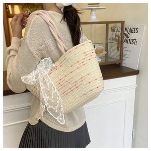 Detail of woven straw bag featuring colorful stitching, lace bow, and large pearl buckle