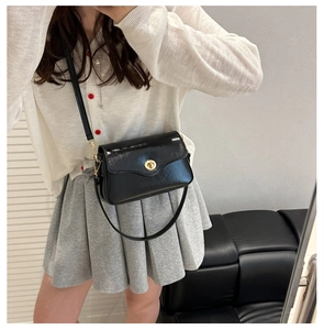 Fashionable black glossy crossbody bag with gold round twist lock on a white sweater
