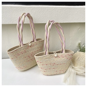 Detail of woven straw tote bag with colorful embroidery and twisted rope handle