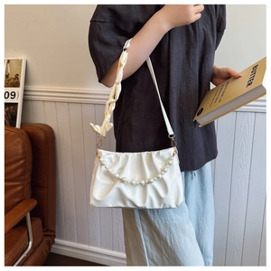 Close-up of white pleated cloud bag with pearl chain and silk bow shoulder strap detail