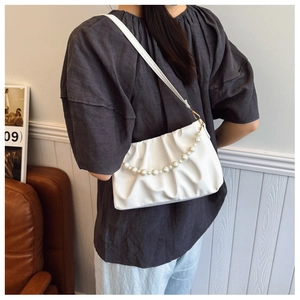 Detail of white pleated cloud bag with pearl strap worn over the shoulder by a model