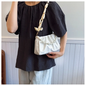 Detailed view of white pleated cloud bag with large pearl chain and silk shoulder strap