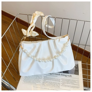 Detailed shot of white pleated shoulder bag with pearl chain and silk strap in a basket