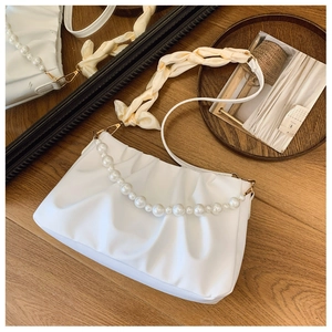 Detail of white pleated cloud bag with elegant pearl chain and woven shoulder strap