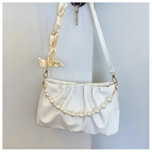 Close-up of white ruched cloud bag featuring pearl chain and yellow silk ribbon strap