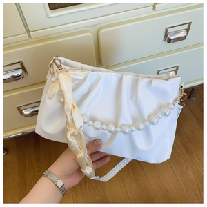 Detail of white pleated cloud bag with pearl chain and silk woven handle on vintage desk