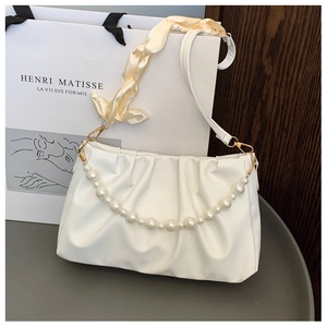 Detail of white pleated cloud bag featuring pearl strap and yellow silk scarf handle