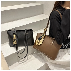 Detail of minimalist leather tote bag featuring contrast stitching and elegant silk scarf