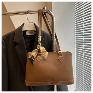 Close-up of a brown tote bag with a decorative silk scarf on a metal hanger