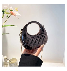 Detail of glossy black quilted crescent handbag with round cutout handle and gold chain