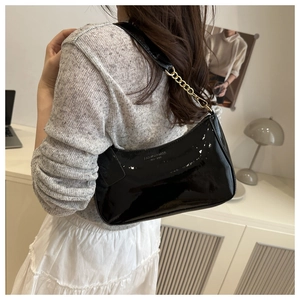 Détail du sac sous l'aisselle en cuir verni noir avec chaîne dorée et texte de mode