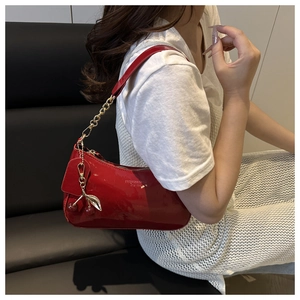 Détail du sac à épaule en cuir verni rouge avec chaîne dorée et breloque cerise
