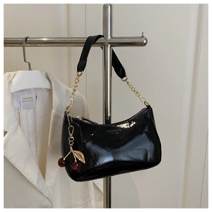 Détail du sac baguette noir brillant avec chaîne dorée et pendentif cerise élégant