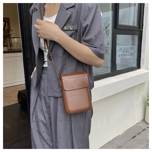 Brown leather crossbody phone bag shown on shoulder over a stylish grey blazer