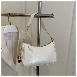 Détail d'un sac d'épaule en cuir verni blanc avec chaîne dorée et breloque cerise