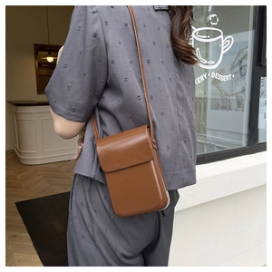 Close-up of a vintage brown leather mini crossbody bag worn by a model in a cafe