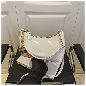 Détail d'un sac à bandoulière blanc en forme de croissant avec breloque cerise