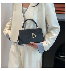 Detail of elegant black glitter clutch bag with gold V-logo and metal chain strap