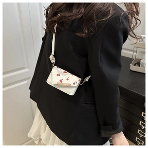 Detail of white mini crossbody bag with cherry print and golden lock worn by a model