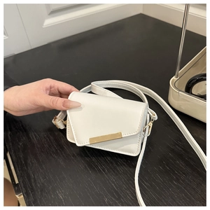 Detail of white leather crossbody bag featuring geometric flap and gold metal bar buckle