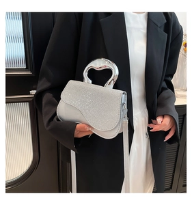 Detail of silver sparkling mini bag with crystal flap and curved metal handle held by model