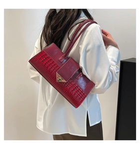Détail d'un sac à main bordeaux à motif crocodile avec boucle dorée triangulaire