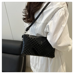 Fashionable black faux leather crossbody bag featuring stylish rivet details on the model