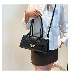 Détail d'un sac à main noir en simili cuir avec texture crocodile et fermoir doré en V