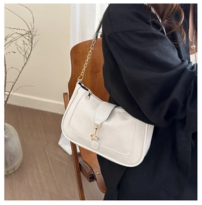 Detail of elegant cream shoulder bag with golden piston clasp and chain strap