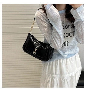Detail of glossy black shoulder bag featuring gold chain strap and buckle on model