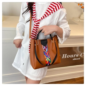 Detail einer braunen Leder-Eimertasche mit buntem Webriemen und einem eleganten schwarzen Griff