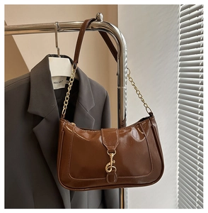 Detail of glossy brown leather crescent bag featuring a golden piston clasp and chain strap